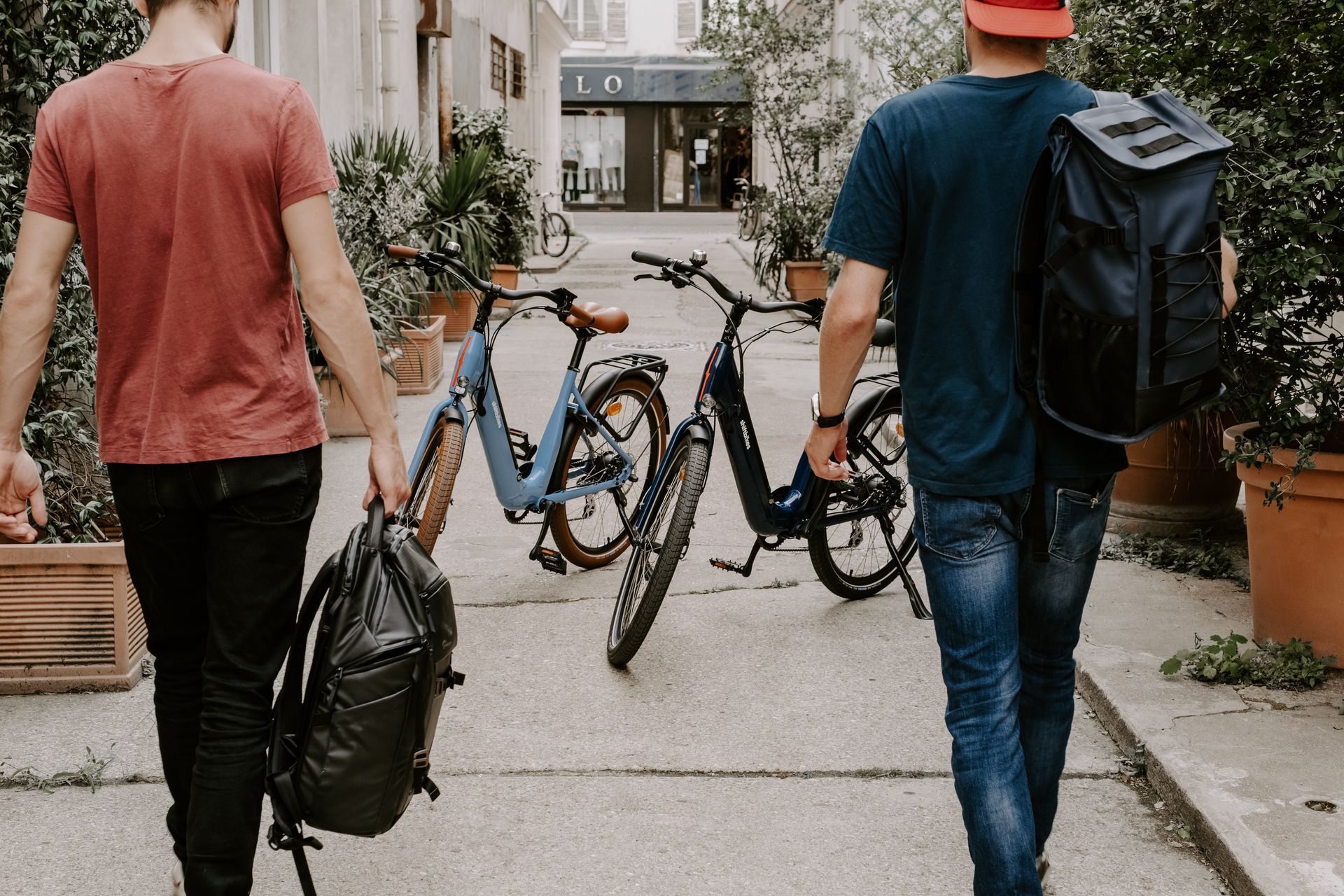 deux hommes marchent avec leurs sac à dos en direction des vélos de location