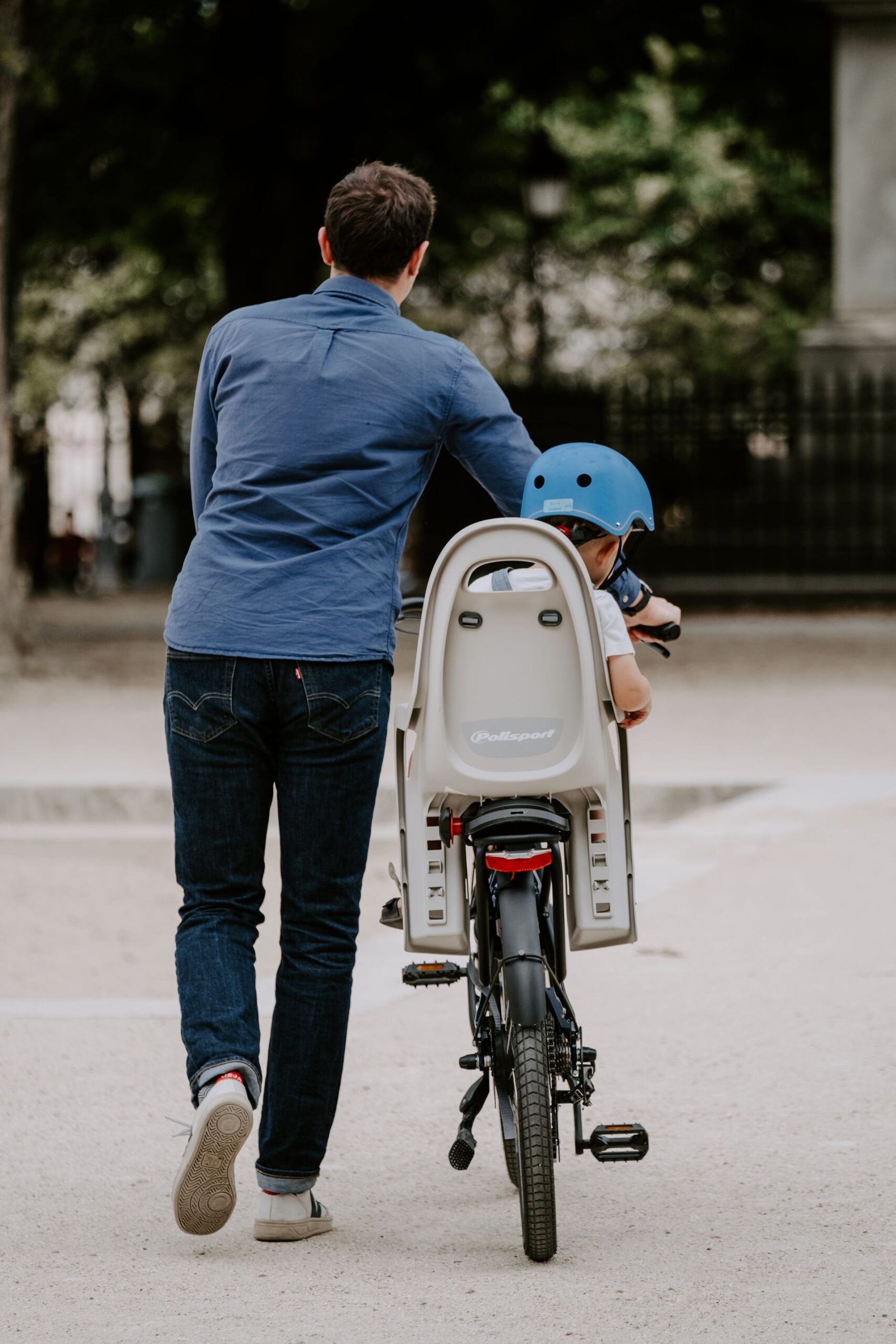 vue de dos d'un père qui marche avec son vélo de location sur lequel est assis son jeune fils